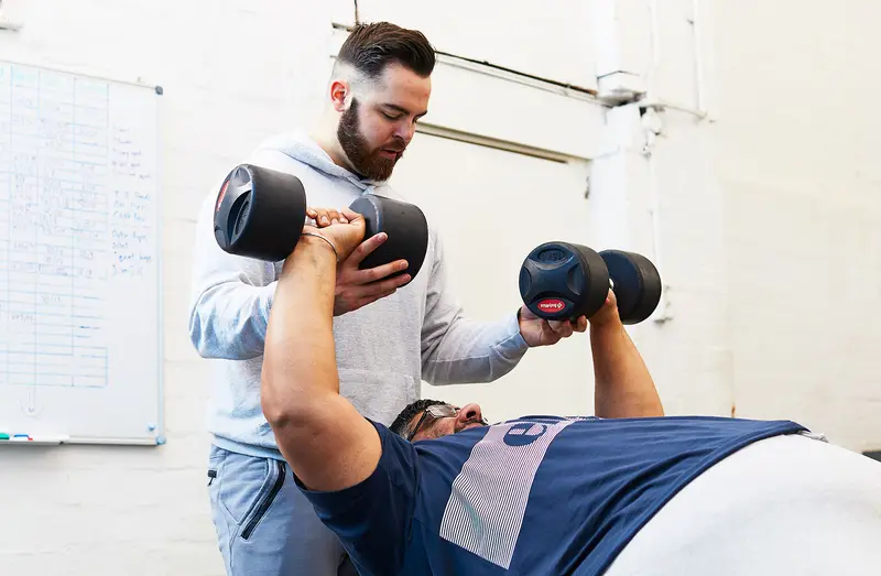 A Transformation Fit coach spotting a member's dumbbell press
